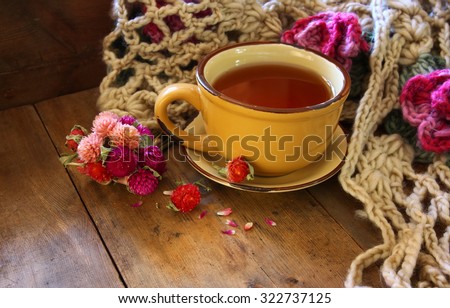Cup of tea with dry flowers and a warm scarf on wooden table