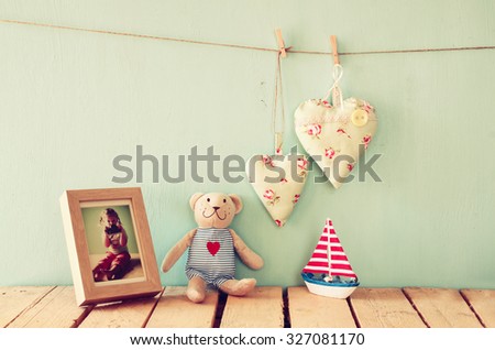 wooden boat toy and teddy bear over wood table next to photo frame with kid\'s old photography and fabric hearts. retro filtered image
