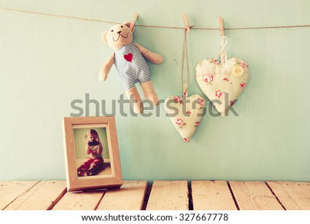 teddy bear over wood table next to photo frame with kid\'s old photography and fabric hearts. retro filtered image