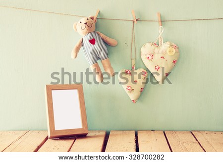 teddy bear over wood table next to photo frame and fabric hearts. retro filtered image