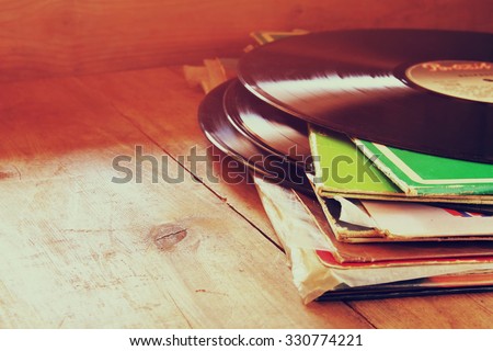 selective focus of records stack with record on top over wooden table. vintage filtered