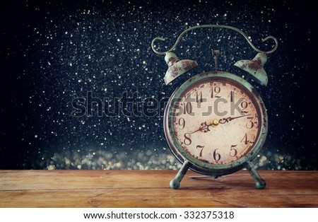 image of vintage alarm clock on wooden table in front of magical glitter silver and black lights background. retro filtered