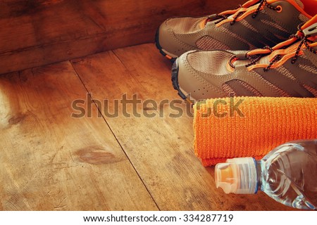 fitness concept with bottle of water, towel and sport footwear over wooden background