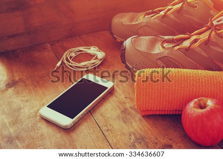 fitness concept with mobile phone with earphones, towel, apple and sport footwear over wooden background. retro filtered