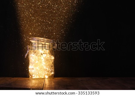low key and vintage filtered image of fairy lights in mason jar with. selective focus. glitter overlay