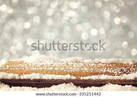 image of wooden old table and december fresh snow on top. in front of glitter background