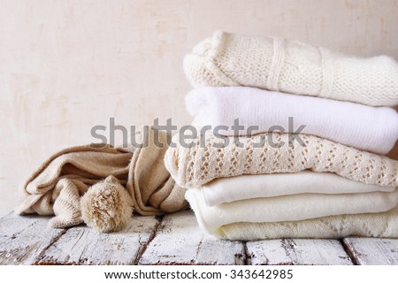 Stack of white cozy knitted sweaters on a wooden table