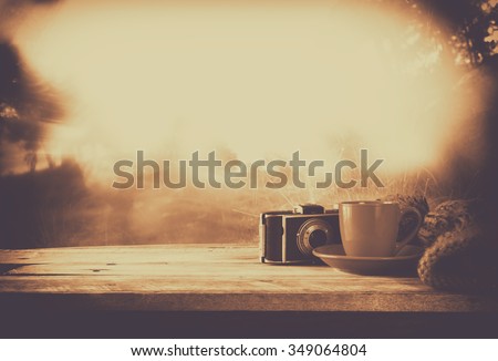 selective focus and abstract photo of cozy knitted hat with to cup of coffee next to old photo camera on a wooden table. faded style retro filtered and toned