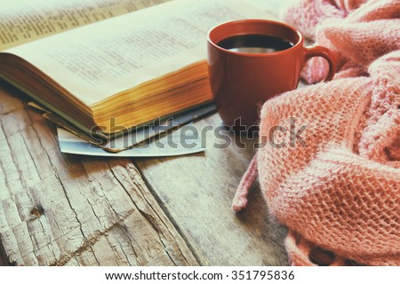selective focus photo of pink cozy knitted scarf with to cup of coffee and open book on a wooden table. style retro filtered