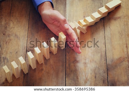 a male hand stoping the domino effect. retro style image executive and risk control concept