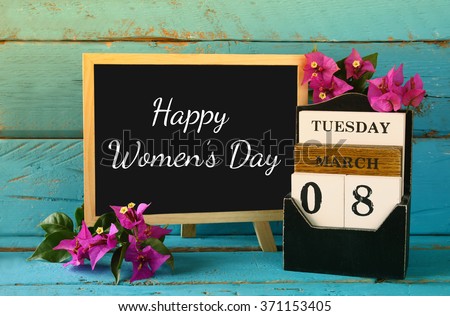 wooden March 8 calendar, next to purple flowers on old blue rustic table. selective focus. vintage filtered. Happy International Women\'s Day concept