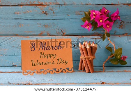 vintage card with phrase: 8 march happy womens day on wooden texture table next to purple bougainvillea flower.