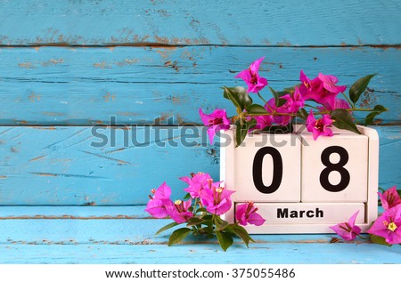 wooden March 8 calendar, next to purple flowers on old blue rustic table. selective focus