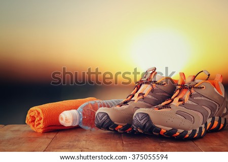 fitness concept with sport footwear, towel and water bottle over wooden table in front of sunset landscape.