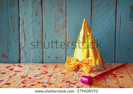 party hat next to pink party whistle on wooden table with colorful confetti. vintage filtered image