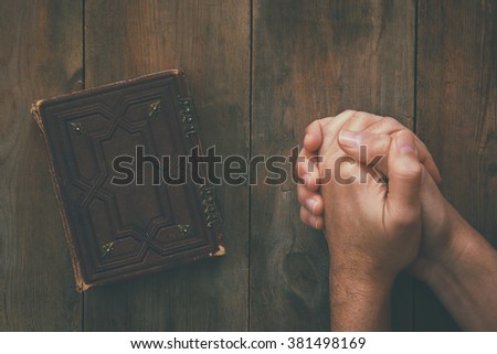 top view image of mans hands folded in prayer next to prayer book. concept for religion, spirituality and faith. vintage filtered and toned