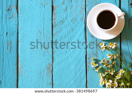 top view image of daisy flowers next to cup of coffee on blue wooden table. vintage filtered and toned