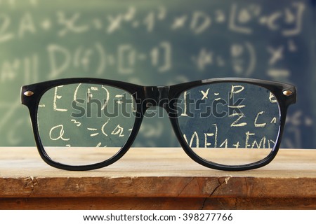 hipster glasses on a wooden rustic table in front blackboard with math formulas and calculation. vintage filtered
