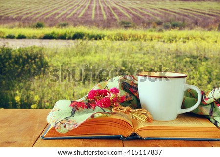 fashion scarf with cup of coffee and old book on a wooden table in front of summer field landscape. vintage filtered