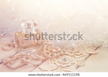 Dreamy photo of white pearls necklace and perfume bottle on toilette table. Selective focus. Glitter overlay