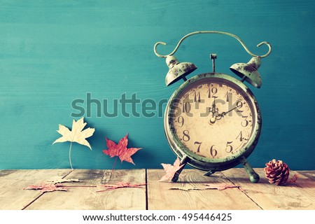 Image of autumn Time Change. Fall back concept. Dry leaves and vintage alarm Clock on  rustic wooden table