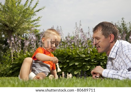 Child and father playing chess in the garden