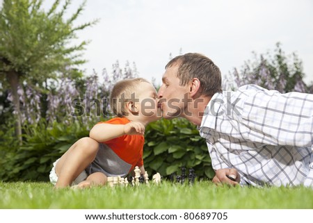 Kissing and playing chess (baby and father kissing over a session of chess in the garden)
