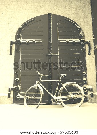 This is a picture of an old door in a castle. These were the doors to the horse stalls. It is winter and an old bike is leaning against the door.