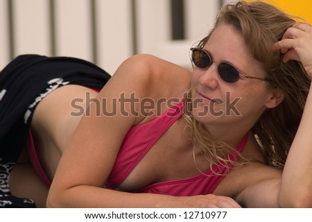 Pretty young woman lounging by the pool in pink bikini.