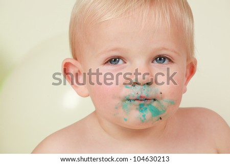 Naughty blond hair,blue eyed boy staring to the right.with blue icing and chocolate birthday cake messed all over his face.