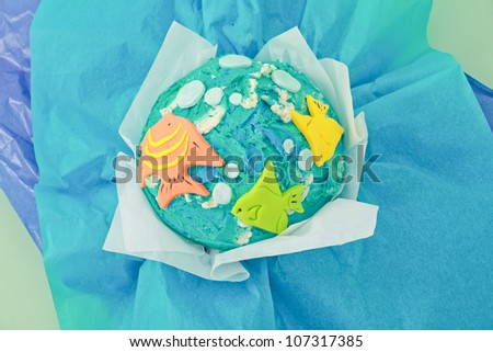 Beautifully designed under the sea fish themed birthday giant cupcake with blue icing yellow fish and white bubbles with light and dark blue tissue crinkle paper isolated on white seamless background
