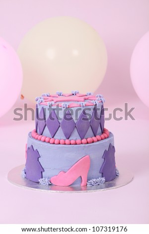 Beautifully designed and decorated two double tier princess themed birthday cake with purple and pink butter and fondant icing featuring beads shoes crown and diamonds on pink background with balloons