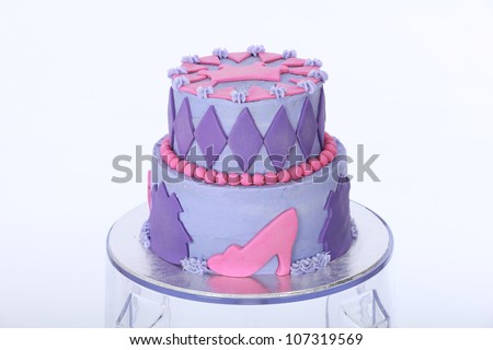 Beautifully designed and decorated two double tier princess themed birthday cake with purple and pink butter and fondant icing featuring beads shoes crown and diamonds on clear acrylic bar stool stand