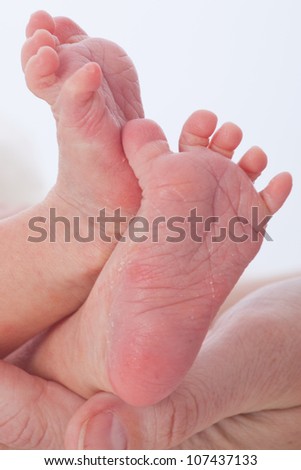 Tiny newborn infant male or female baby feet and toes held gently in mothers hands on soft white fury blanket