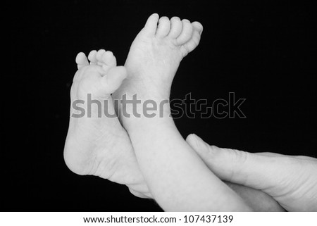 Tiny newborn male or female infant baby feet and toes held gently in mothers hands in black and white