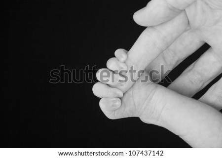 Tiny little newborn infant baby hand holding or clasping mother or fathers finger in black and white