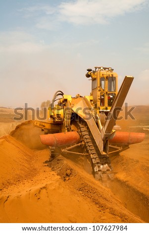 Yellow  and orange Vermeer trencher industrial machine digging trench or ditch outside in red sand or dirt on construction site for new pipe line