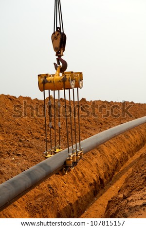 Large yellow side boom pipe layer or stringer industrial machine on orange dusty sandy outdoor construction site laying a pipe in a trench