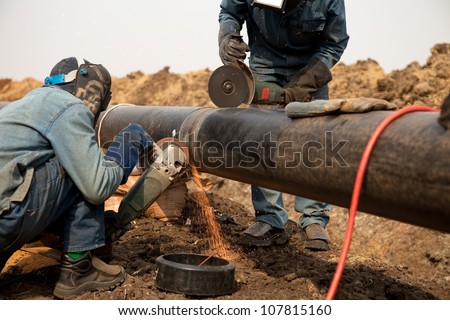Male welder worker wearing protective clothing fixing welding and grinding industrial construction oil and gas or water plumbing pipeline outside on site