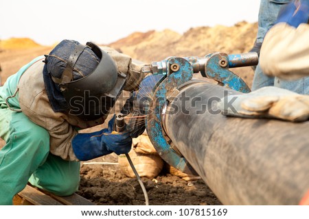 Male welder worker wearing protective clothing fixing and joining industrial construction oil and gas or water plumbing pipeline using an external pipe clamp outside on site