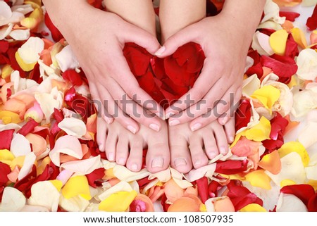 Neat tidy and clean hands and feet which are well manicured in a spa, resting on a bed of rose petals and making a red heart with hands.