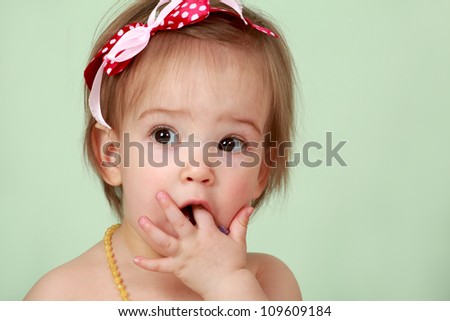 Cute little baby girl sitting on isolated seamless green background eating cake with hands by mouth and with pretty red and white polka dot ribbon bow in hair