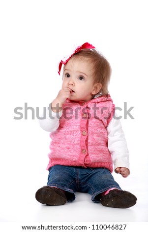 Adorable baby girl wearing blue jeans and pink top with pretty bow in hair isolated on a white seamless background