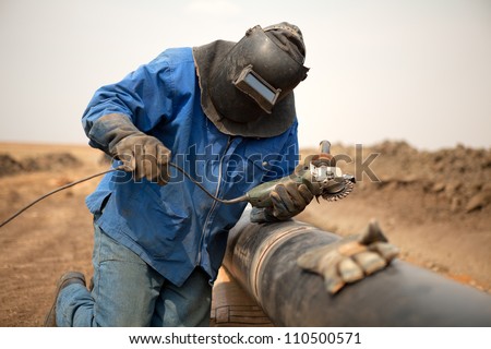 Male welder worker wearing protective clothing fixing welding and grinding industrial construction oil and gas or water and sewerage plumbing pipeline outside on site