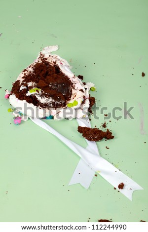 Smashed up birthday party cake in a heaped mess on the green floor
