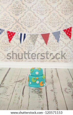 Beautiful round double tier blue green and orange polka dot birthday party cake on vintage wallpaper background and distressed white washed wooden floor