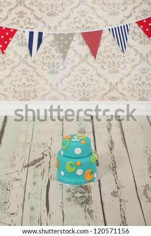Beautiful round double tier blue green and orange polka dot birthday party cake on vintage wallpaper background and distressed white washed wooden floor
