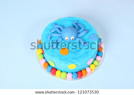 Kids blue round birthday party cake with red, yellow, blue and pink polka dots and cute blue fondant octopus on top. All on blue background with balloons and flag bunting.