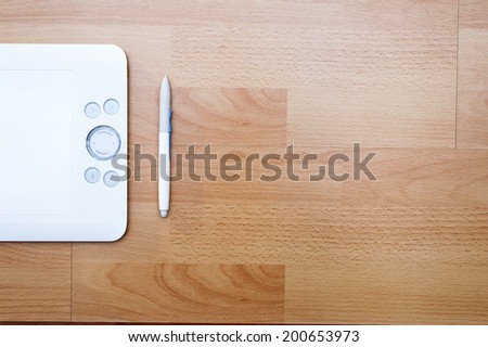 White graphic tablet with a pen on wooden laminated floor background