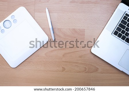White graphic tablet with a pen on wooden laminated floor background